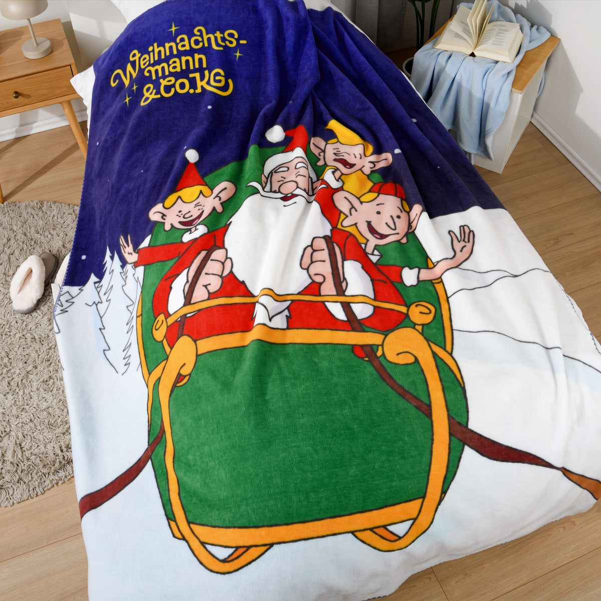 Kuscheldecke mit dem Weihnachtsmann und seinen Elfen im Schlitten auf einem Bett
