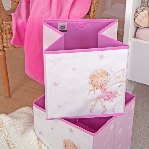Zwei Aufbewahrungsboxen ‘Little Fairy’ übereinander auf dem Boden vor einem Korbstuhl mit pinker Decke, die obere halb zusammengefaltet mit sitzender Fee