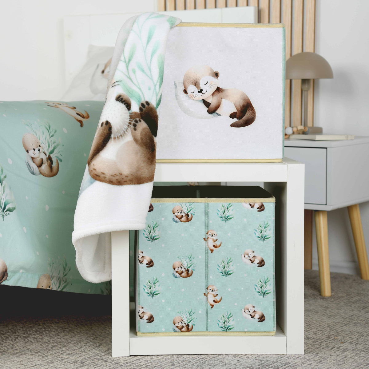 Aufbewahrungsbox ‘Schnuffel-Otter’ mit schlafendem Otter auf einem weißen Regalwürfel, darin eine zweite Box mit der gemusterten Seite, über der oberen Box hängt eine Decke