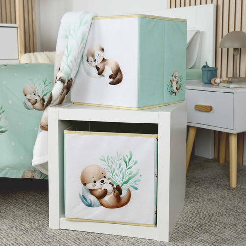 Zwei Aufbewahrungsboxen ‘Schnuffel-Otter’ auf und in einem weißen Regalwürfel, oben der schlafende Otter, unten der Otter mit weißer Kugel
