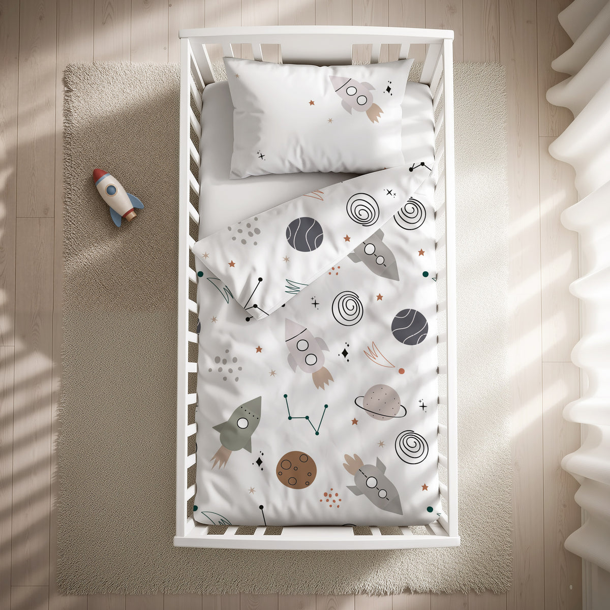 babybest Bettwäsche-Set ‘Weltall’ 100 x 135 cm mit Kissenbezug 40 x 60 cm im Gitterbett, Draufsicht mit umgeschlagenem Bettbezug