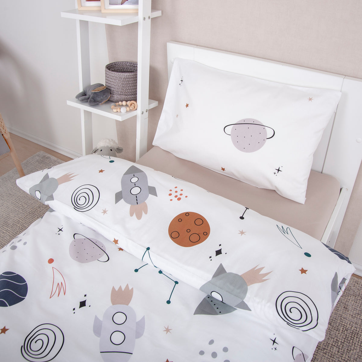 Kissenbezug ‘Weltall’ mit der Planeten-Seite auf einem Kinderbett, darunter der Bettbezug mit Raketen und Planeten
