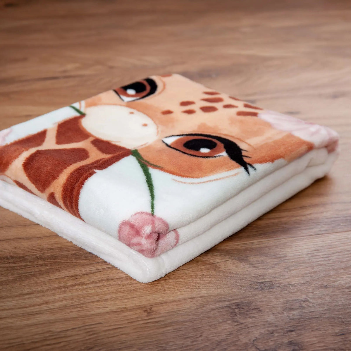 Zusammengelegte Kuscheldecke ‘Giraffe’ auf dem Holzboden