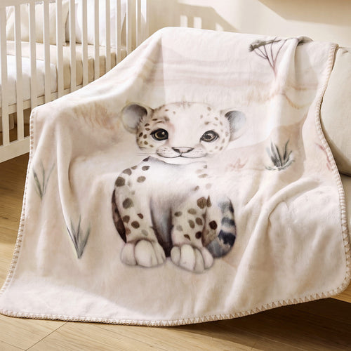 babybest Kuscheldecke ‘Kleiner Leo’ über einem hellen Sofa vor einem weißen Babybett