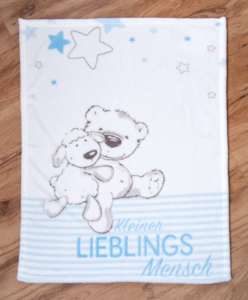 Kuscheldecke ‘Kleiner Lieblingsmensch’ in Blau ausgebreitet auf einem Holzboden