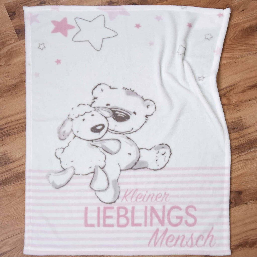 Kuscheldecke ‘Kleiner Lieblingsmensch’ in Rosa ausgebreitet auf einem Holzboden
