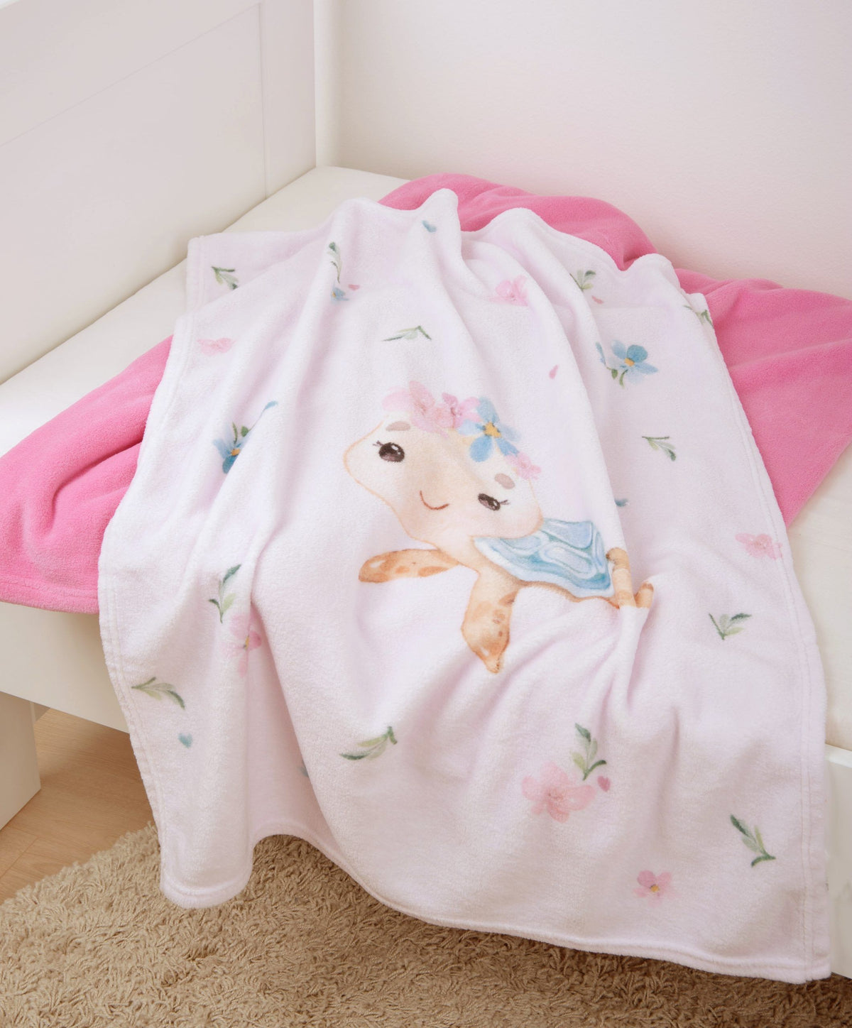 babybest Kuscheldecke ‘Little Turtle’ locker über eine weiße Sitzbank mit pinker Decke gelegt