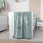 babybest Kuscheldecke ‘Nordic Forest’ über dem Fußteil eines weißen Betts
