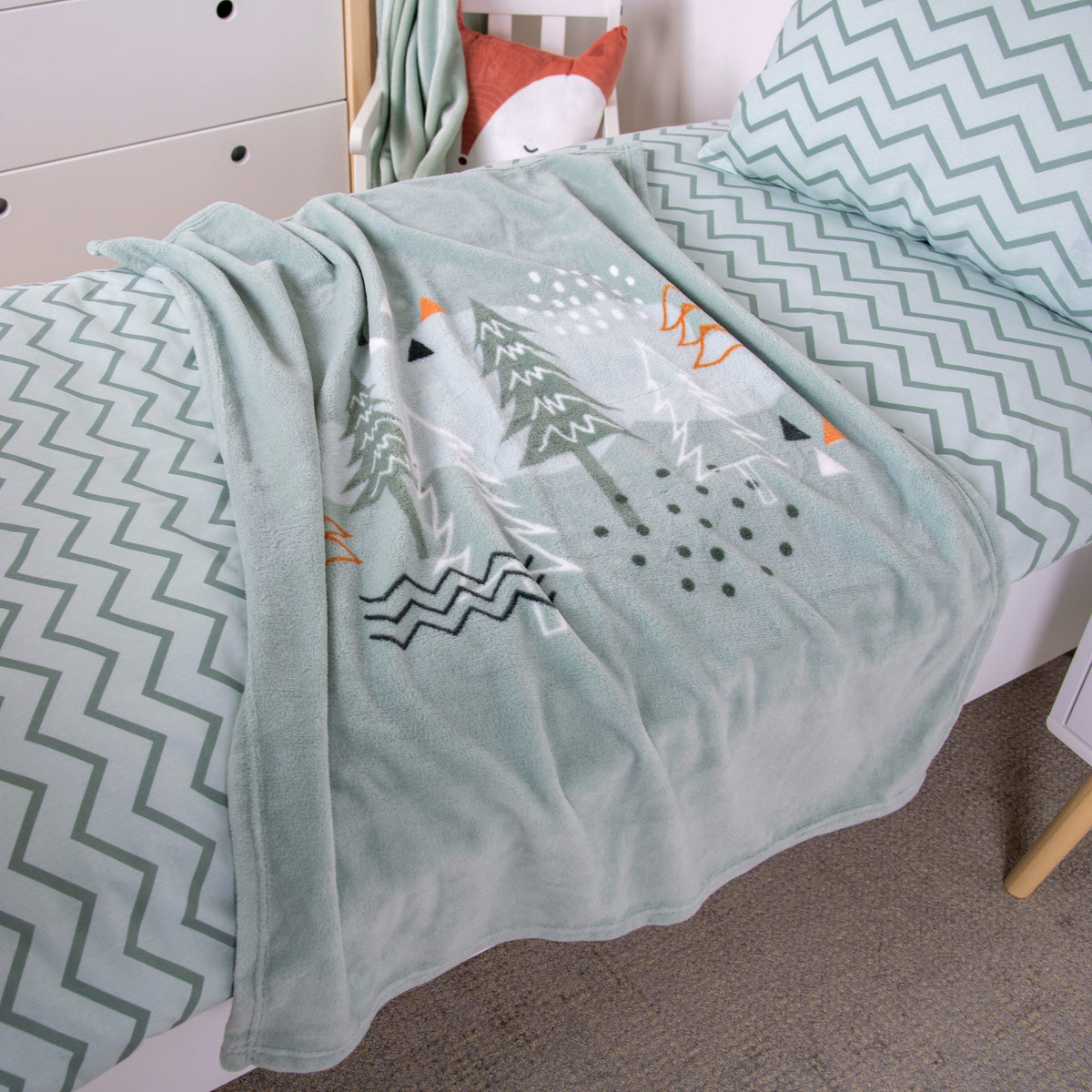 Kuscheldecke ‘Nordic Forest’ auf einem Bett mit Zickzack-Bettwäsche