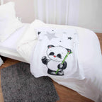 babybest Kuscheldecke ‘Panda’ auf einem weiß bezogenen Bett