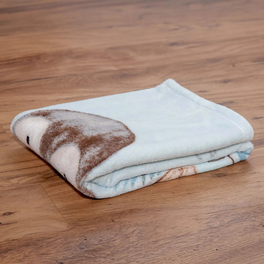 Zusammengelegte Kuscheldecke ‘Pinguin’ auf einem Holzboden