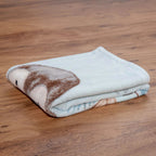 Zusammengelegte Kuscheldecke ‘Pinguin’ auf einem Holzboden