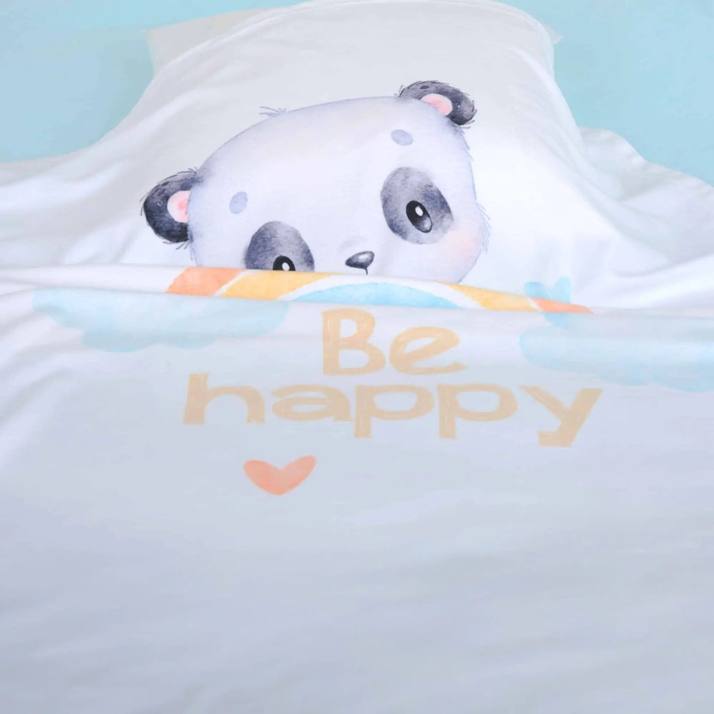 Kuscheldecke ‘Regenbogen Panda’ auf einem Bett mit hellblauem Laken