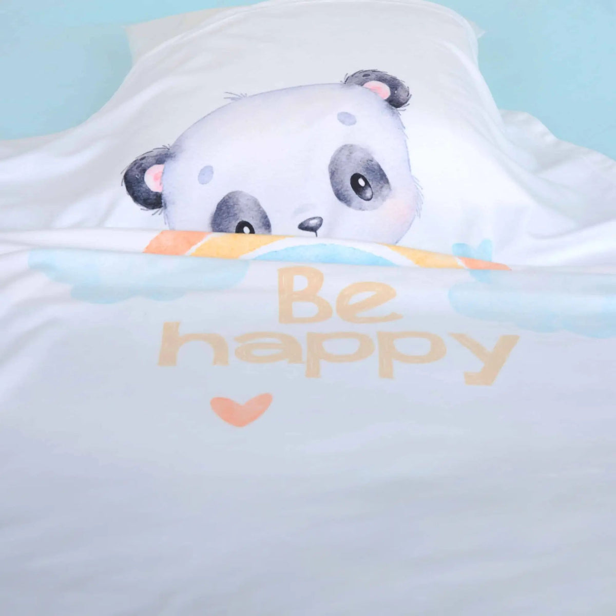 Kuscheldecke ‘Regenbogen Panda’ auf einem Bett mit hellblauem Laken