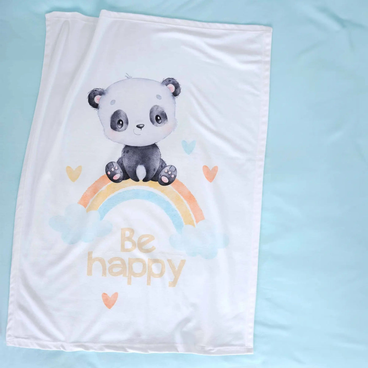 Ausgebreitete Kuscheldecke ‘Regenbogen Panda’ auf hellblauem Laken