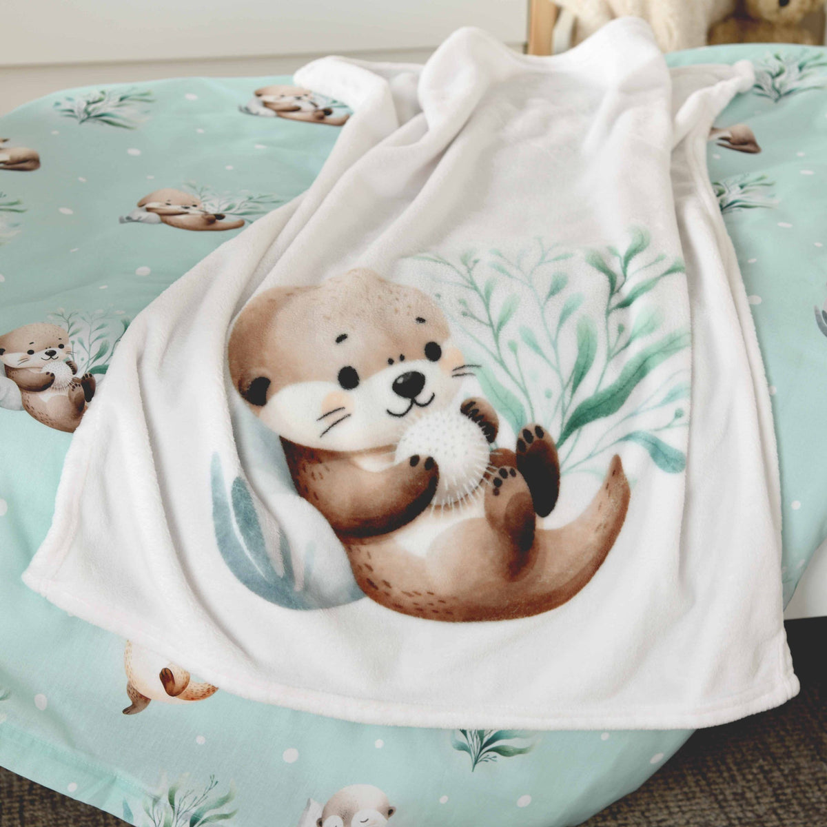 babybest Kuscheldecke ‘Schnuffel-Otter’ auf einem Bett mit mintfarbener Otter-Bettwäsche