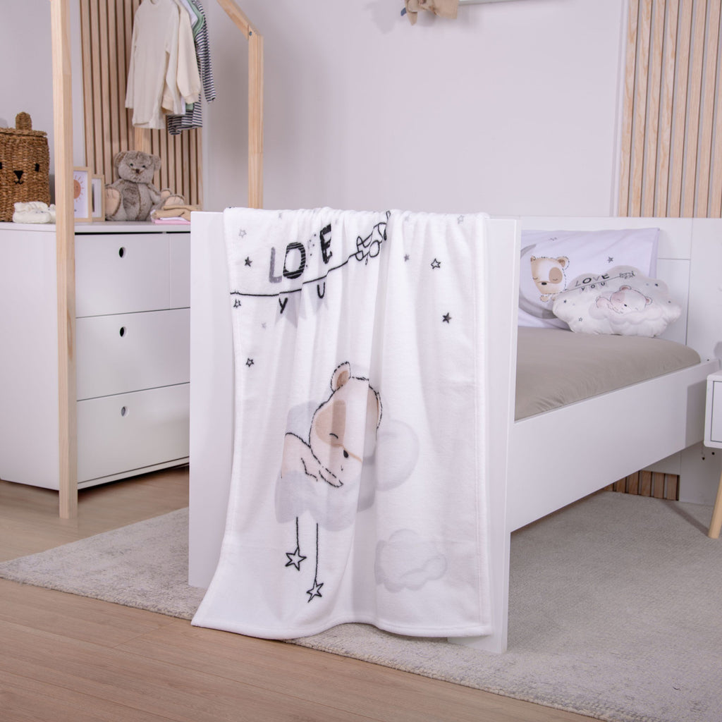babybest Kuscheldecke ‘Sleeping little Bear’ aus Flausch über dem Fußteil eines weißen Betts