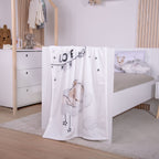 babybest Kuscheldecke ‘Sleeping little Bear’ aus Flausch über dem Fußteil eines weißen Betts