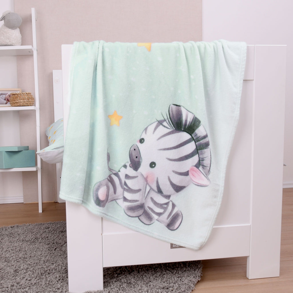 babybest Kuscheldecke ‘Zebra’ über dem Rand eines weißen Babybetts