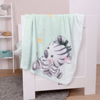 babybest Kuscheldecke ‘Zebra’ über dem Rand eines weißen Babybetts