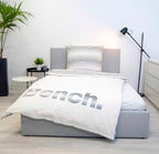 Bench Bettwäsche ‘Gestreift’ auf einem grauen Polsterbett, Logo-Seite