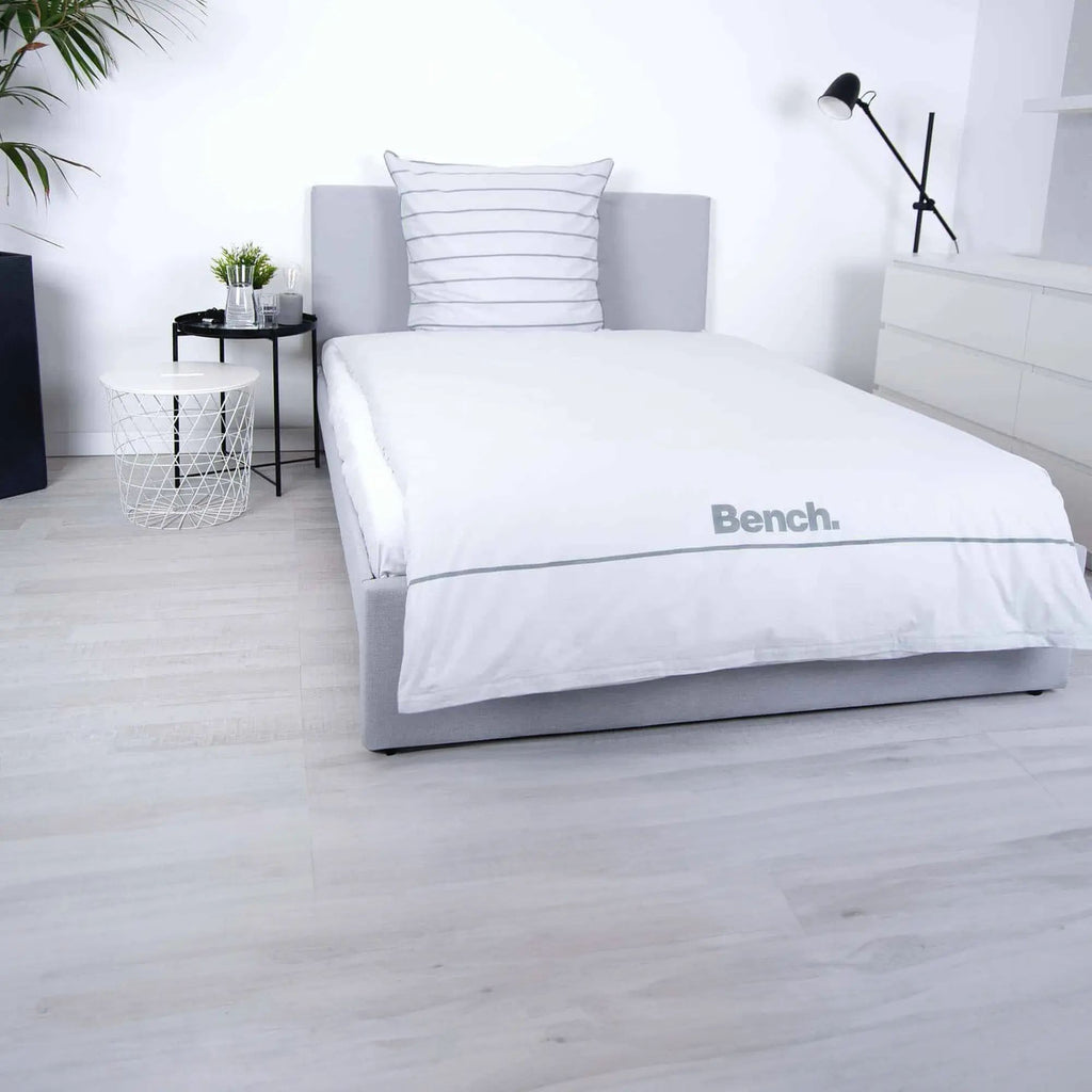Bench Bettwäsche ‘Grau/Gestreift’ auf einem grauen Polsterbett, Logo-Seite