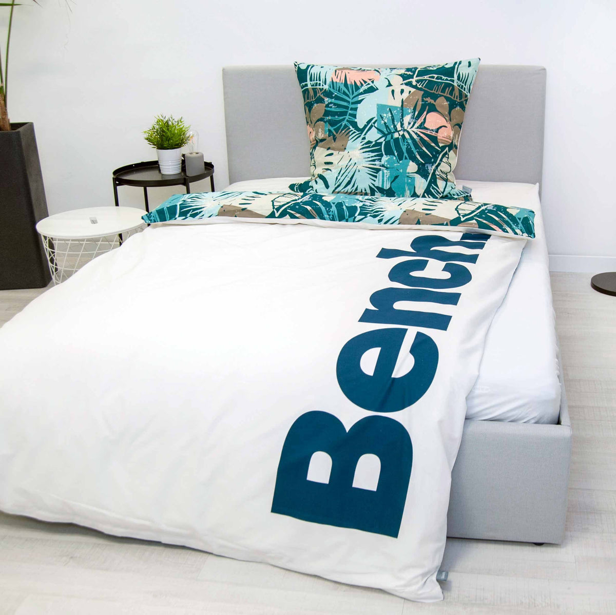 Bench Bettwäsche ‘Hawaii’ auf einem grauen Polsterbett, Logo-Seite mit Blätter-Kissen