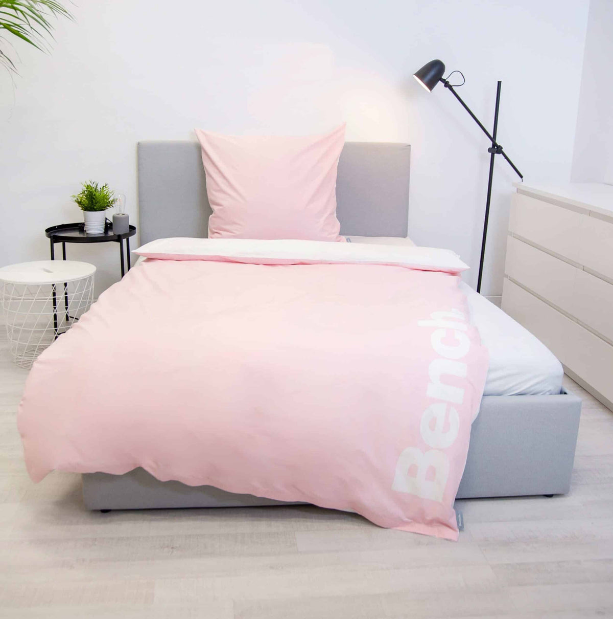 Bench Bettwäsche ‘Hellrosa’ auf einem grauen Polsterbett, rosa Logo-Seite