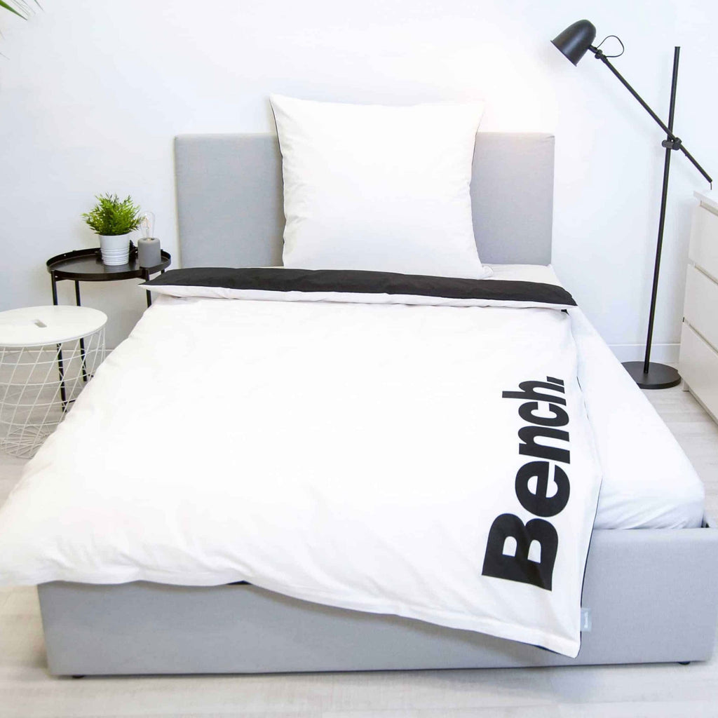 Bench Bettwäsche ‘Schwarz/Weiß’ auf einem grauen Polsterbett, weiße Seite mit schwarzem Logo
