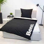 Bench Bettwäsche ‘Schwarz/Weiß’ auf einem grauen Polsterbett, schwarze Seite mit weißem Logo