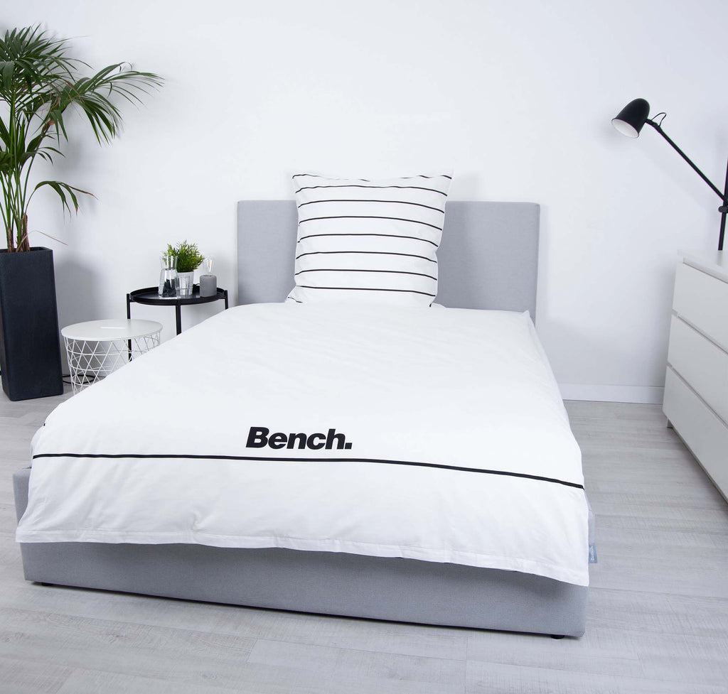 Bench Bettwäsche ‘Weiß/Gestreift’ auf einem grauen Polsterbett, Logo-Seite