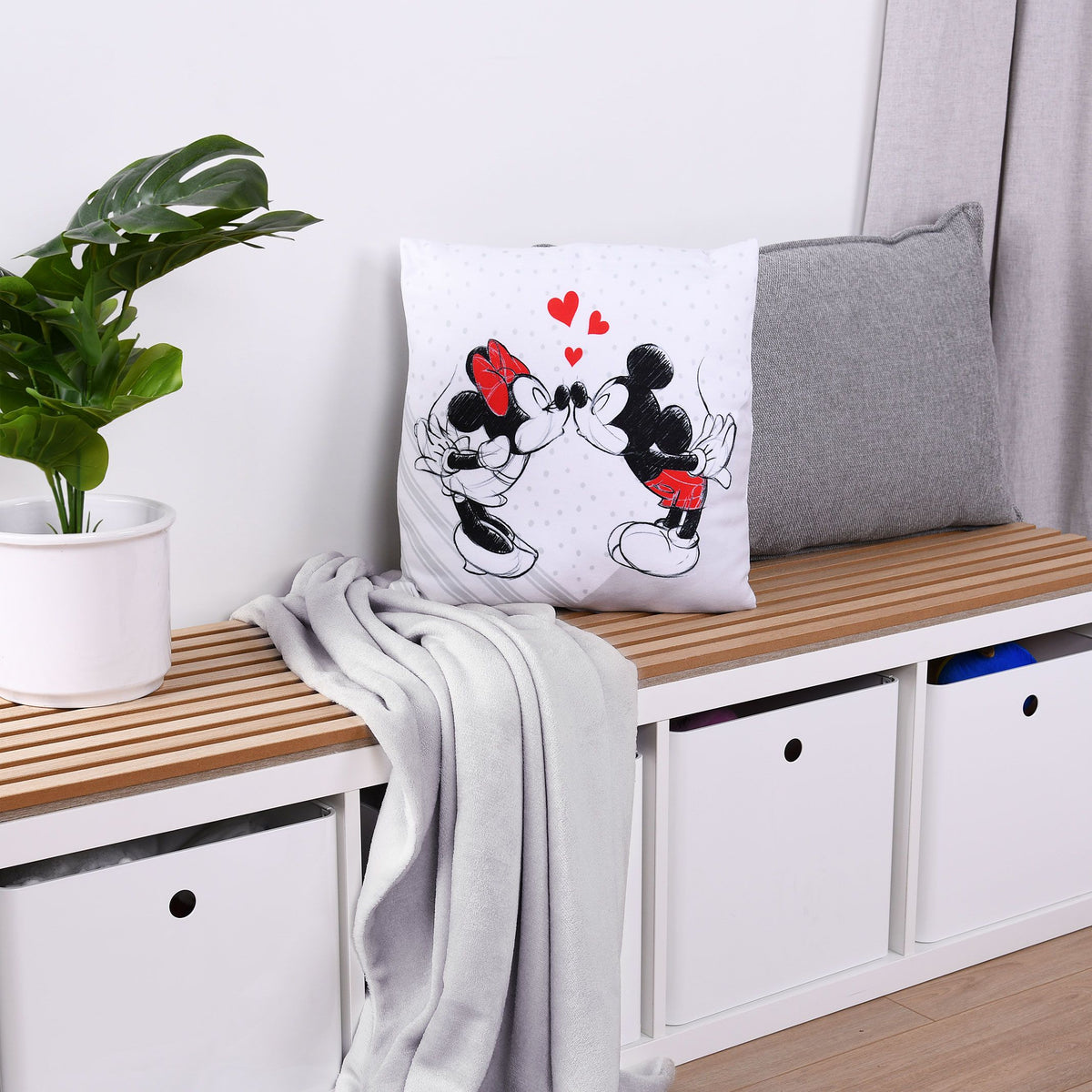 Disney Mickey & Minnie Dekokissen ‘Love’ auf einer Holzbank neben grauem Kissen und Decke