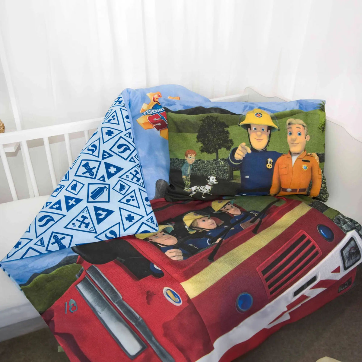 Kissen mit Sam, einem Kollegen im orangefarbenen Overall, einem Jungen und einem Dalmatiner auf dem Bettbezug mit Feuerwehrauto im Gitterbett, links die umgeschlagene hellblaue Wendeseite