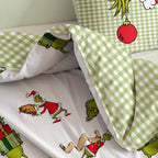 Grinch Winterbettwäsche ‘Merry Grinchmas’ auf dem Bett: Grinch-Figuren auf dem Bettbezug, die Karo-Rückseite umgeschlagen, dahinter der Karo-Kissenbezug mit roter Christbaumkugel