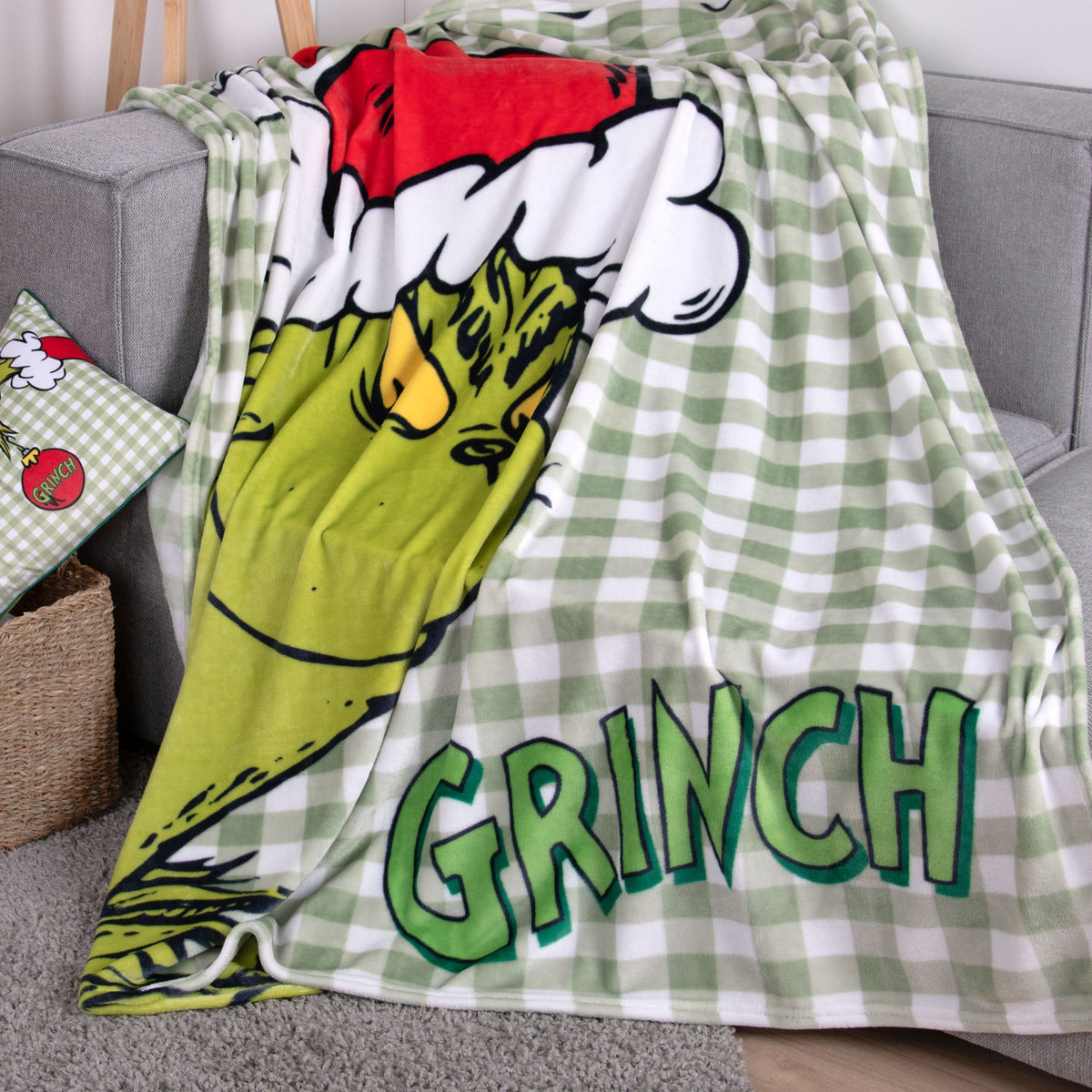 Grinch Kuscheldecke ‘Merry Grinchmas’ auf dem Sofa neben einem Grinch-Kissen