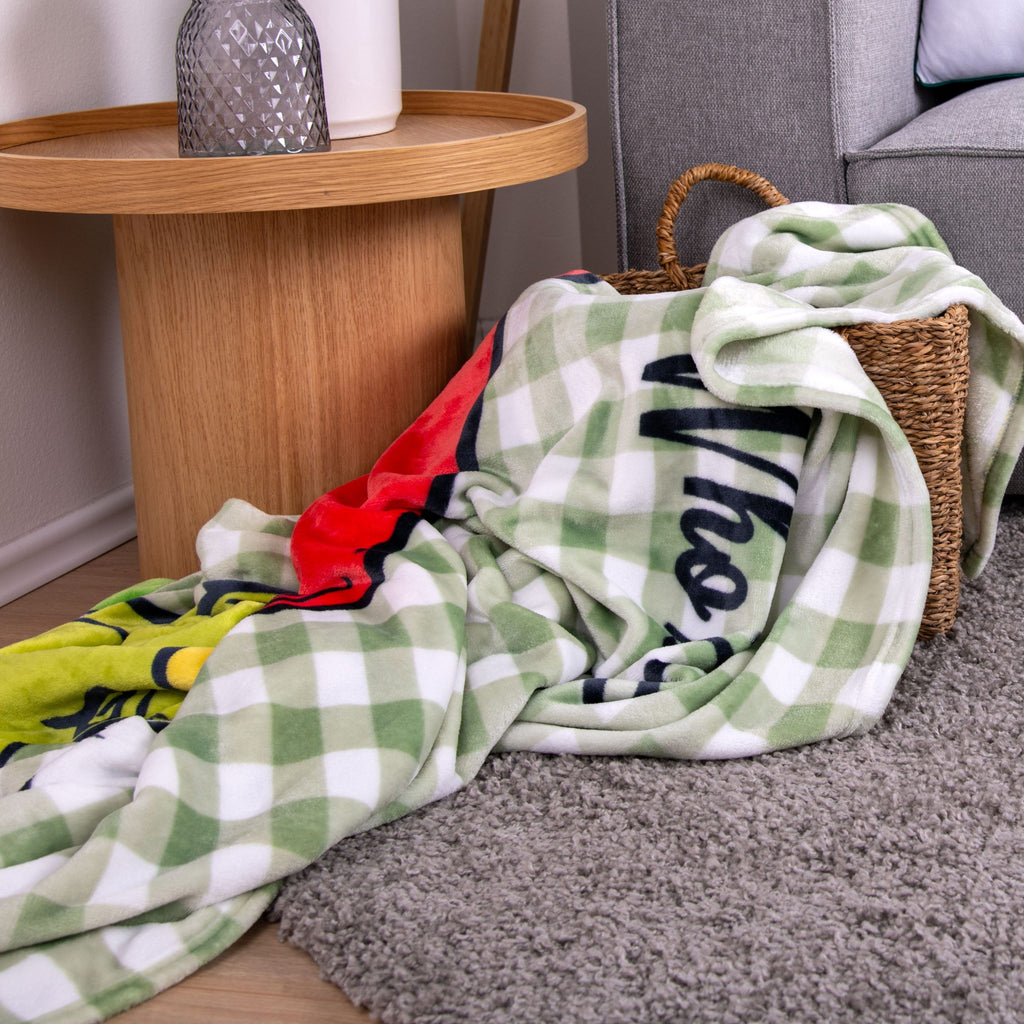 Grinch Kuscheldecke ‘Merry Grinchmas’ locker in einem Korb neben dem Beistelltisch