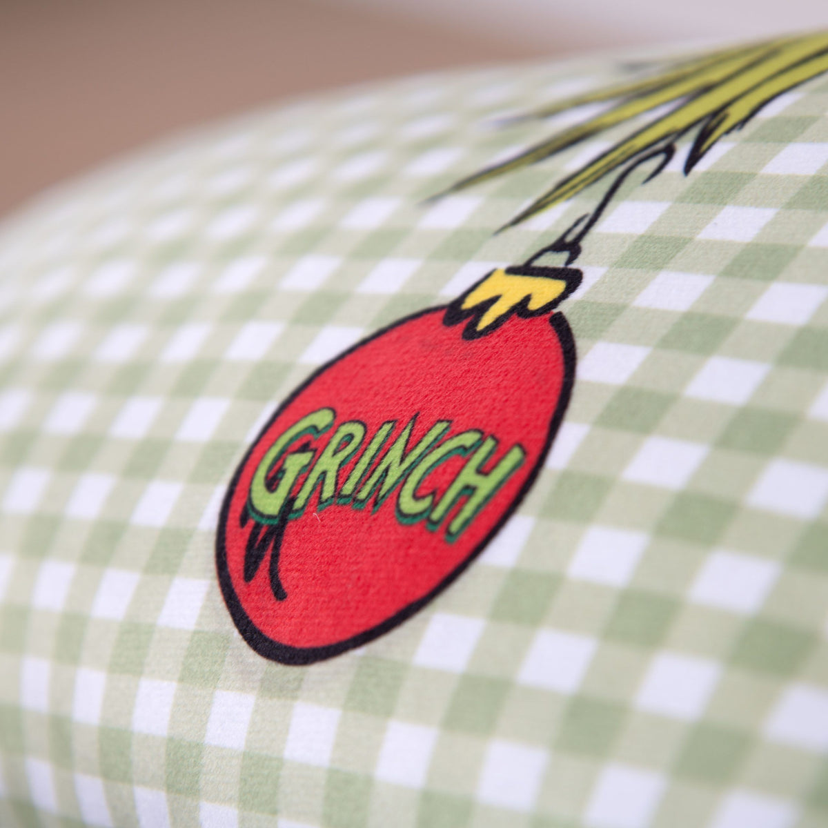 Nahaufnahme der roten Christbaumkugel mit GRINCH-Schriftzug auf dem Karo-Kissen