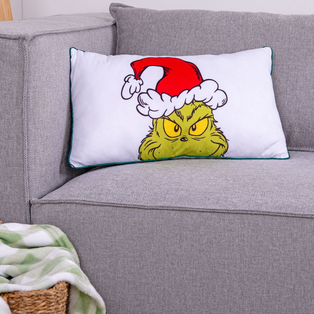 Grinch Kuschelkissen ‘Merry Grinchmas’ auf einem grauen Sofa, Vorderseite mit Grinch-Gesicht