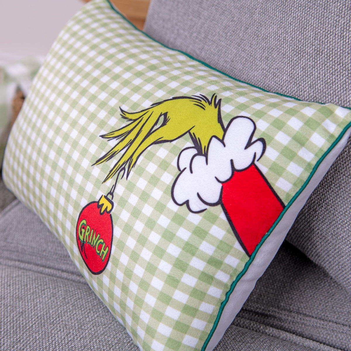 Rückseite des Grinch Kuschelkissens: grün-weißes Karo mit Grinch-Hand und roter Kugel, grüner Kederrand