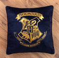 Harry Potter Dekokissen ‘Houses of Hogwarts’ mit goldenem Hogwarts-Wappen auf einem Holzboden