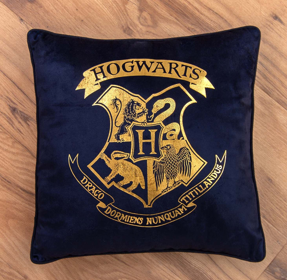 Harry Potter Dekokissen ‘Houses of Hogwarts’ mit goldenem Hogwarts-Wappen auf einem Holzboden