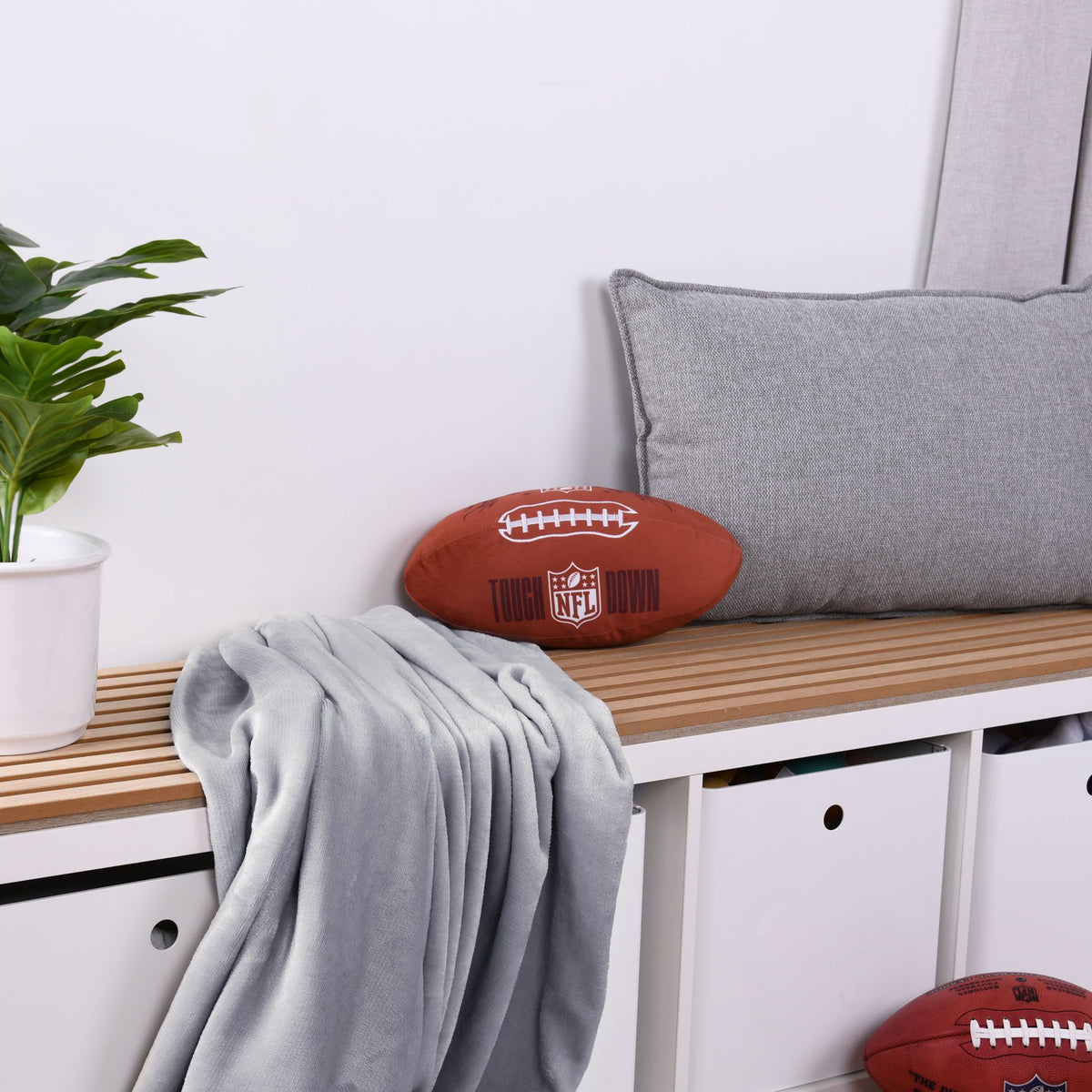 NFL Formkissen ‘Football’ auf einer Holzbank neben grauem Kissen und Decke