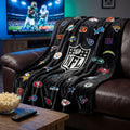 NFL Kuscheldecke ‘All Teams’ über einem Ledersofa vor dem Fernseher beim Football-Abend