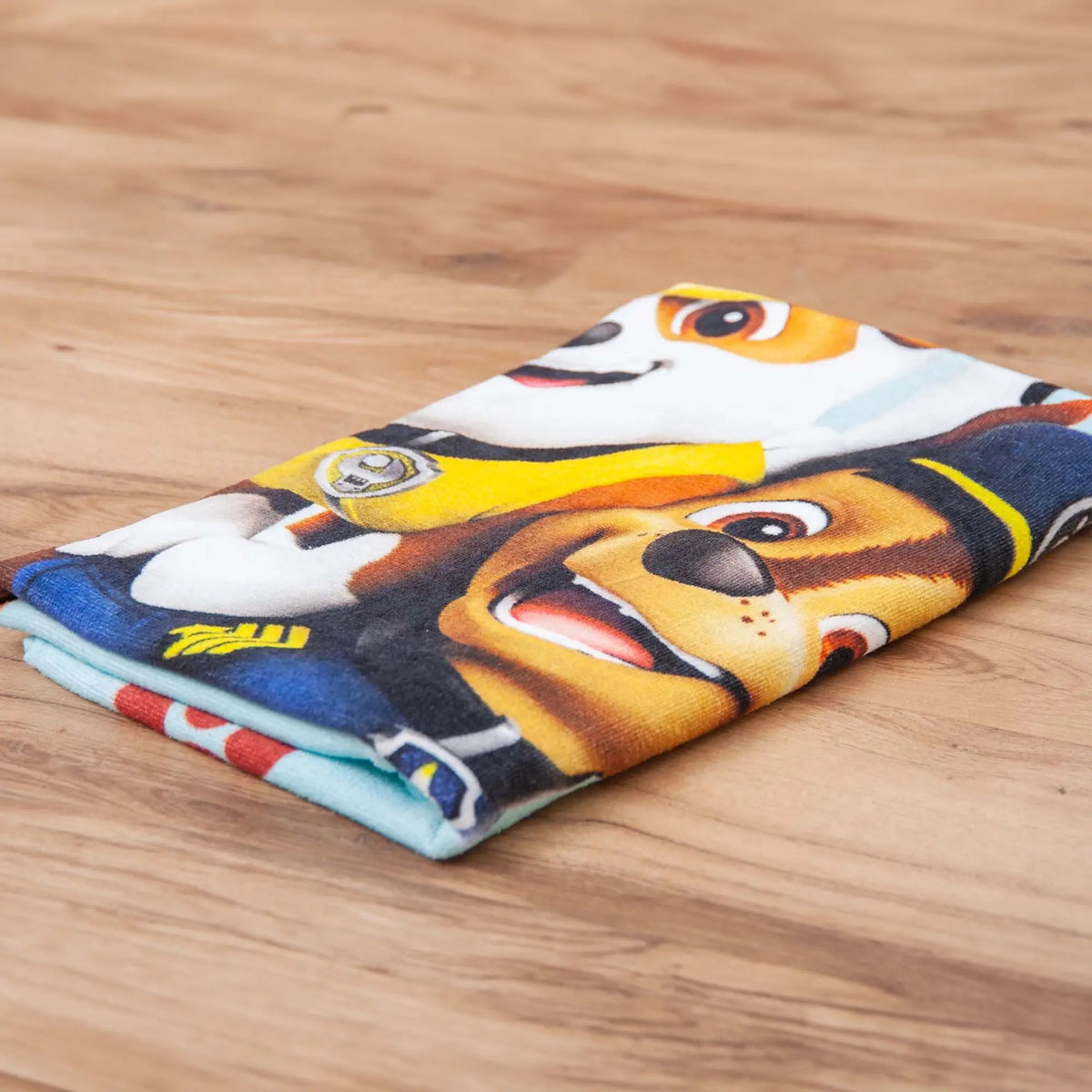 Gefaltetes Paw Patrol Handtuch ‘Friends’ auf Holzboden, Chase und Rubble in Nahaufnahme