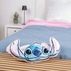 Stitch Kuschelkissen auf einer Holzbank vor einem Bett mit blaugrauer Bettwäsche