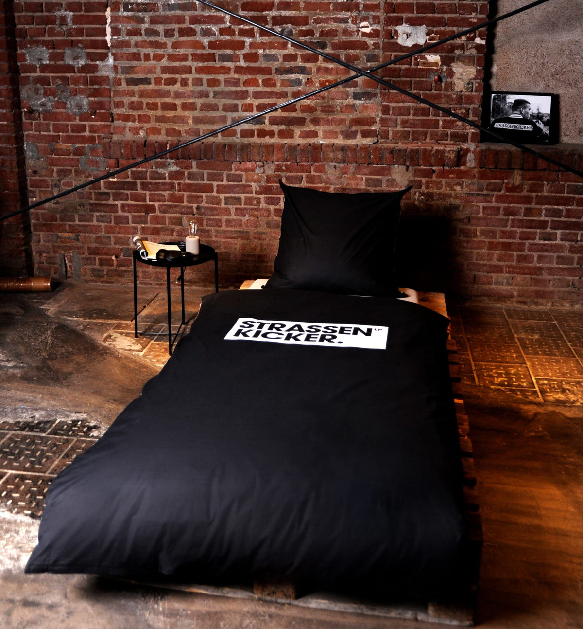 Bett mit der schwarzen Seite der STRASSENKICKER Bettwäsche ‘Grau’ vor einer Backsteinwand