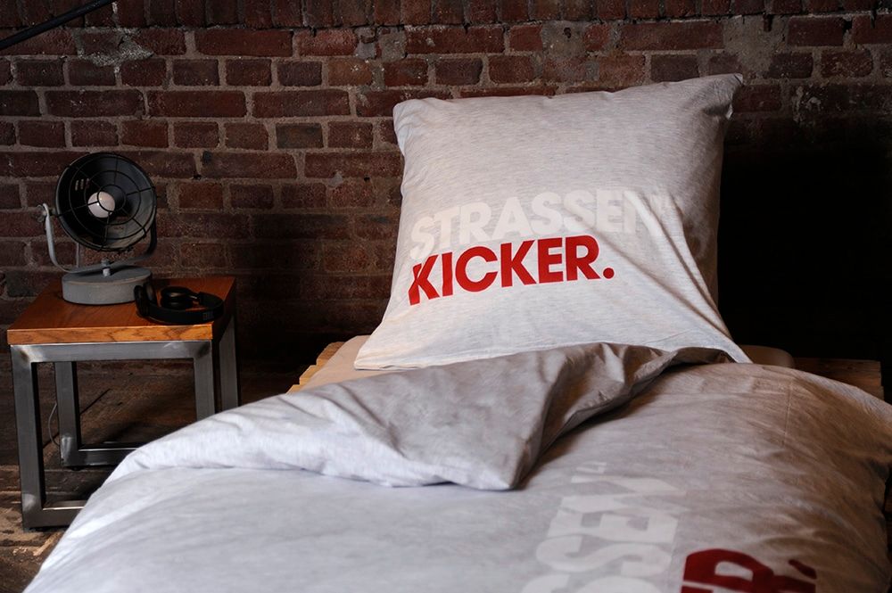 Kissen mit STRASSENKICKER-Logo vor einer Backsteinwand