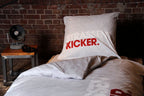 Kissen mit STRASSENKICKER-Logo vor einer Backsteinwand