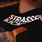 STRASSENKICKER Kuscheldecke auf einem braunen Ledersofa