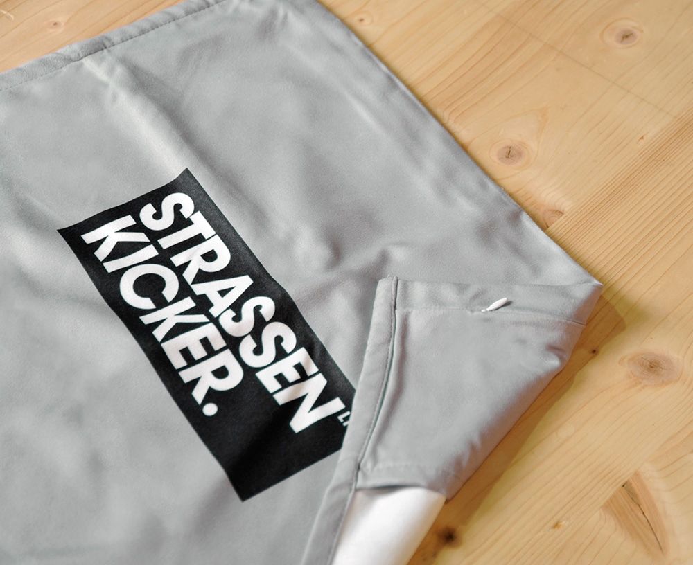 STRASSENKICKER Logo und umgenähter Flap des Fitnesstuchs auf Holzboden